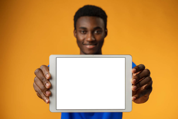 African american man showing blank digital tablet screen with copy space in yellow studio. - Foto, afbeelding