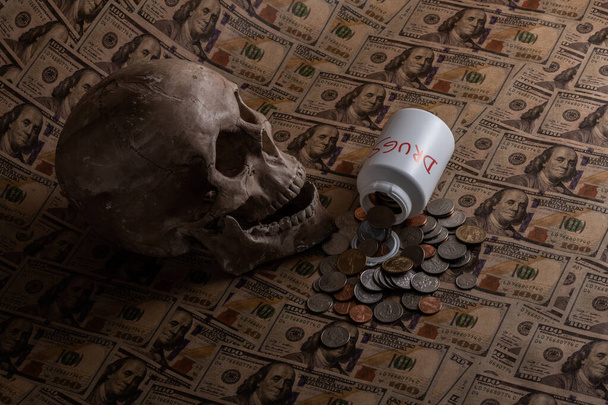 Een plastic container voor drugs met de inscriptie DRUGS, een schedel en Amerikaanse munten op de achtergrond van biljetten van 100 dollar - Foto, afbeelding