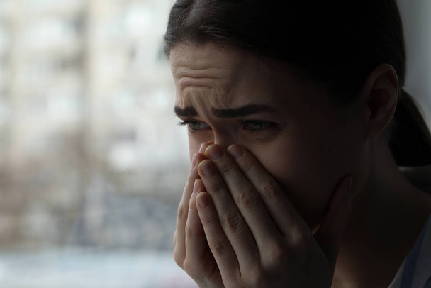 Sad young woman crying near window indoors, closeup with space for text. Loneliness concept - Φωτογραφία, εικόνα