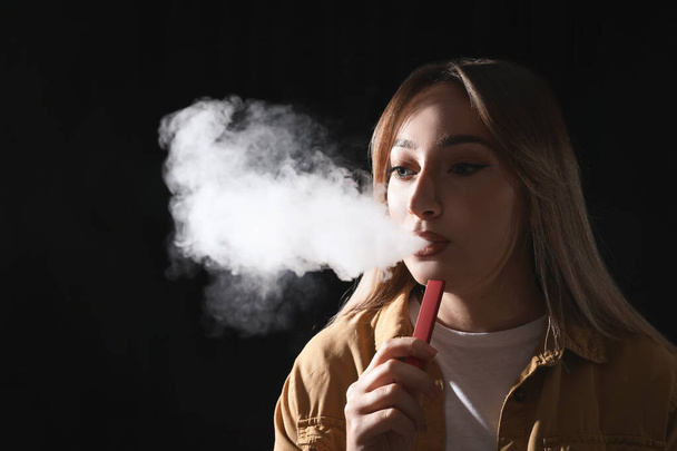 Young woman using electronic cigarette on black background - Foto, Imagem