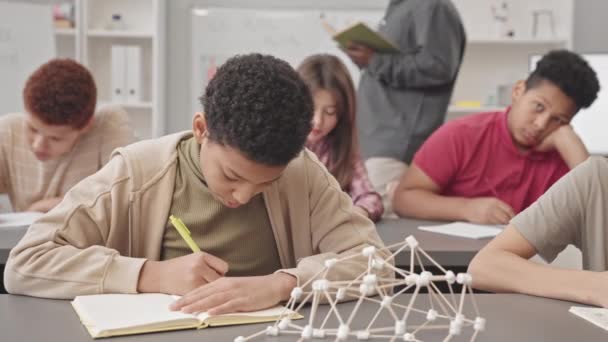 Waist up shot of diverse middle school boys and girls taking notes in their copybooks having Science lesson in modern classroom - Footage, Video