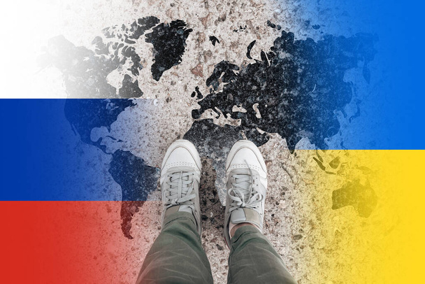 Widok z góry żeńskich nóg w tenisówkach na tle ukraińskich i rosyjskich flag narodowych z mapą świata. Ukraina kontra Rosja w kontekście kryzysu światowego - Zdjęcie, obraz