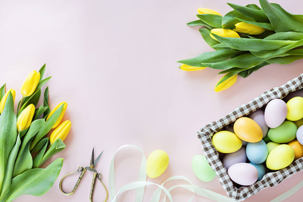 Stylish background with colorful easter eggs isolated on pastel pink background with yellow tulip flowers. Flat lay, top view, mockup, overhead, template - 写真・画像