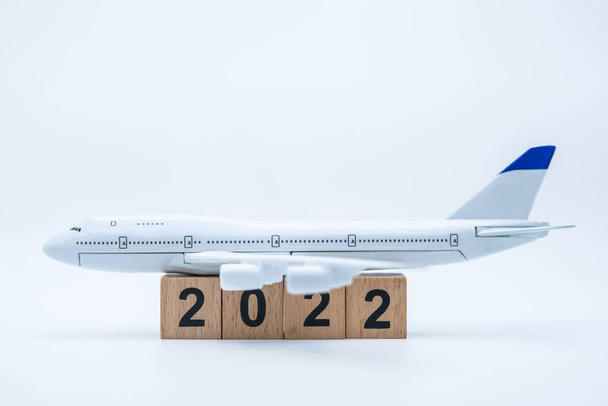 Neujahr 2022 und Reisekonzept. Nahaufnahme eines Flugzeugspielzeugmodells auf einem Stapel hölzerner Zahlenblöcke auf weißem Hintergrund. - Foto, Bild