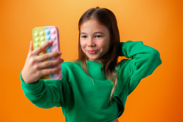 Cute teen girl using mobile phone with positive expression against orange background - Valokuva, kuva