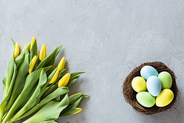 Stylish background with colorful easter eggs isolated on gray concrete background with yellow tulip flowers. Flat lay, top view, mockup, overhead, template - Photo, image