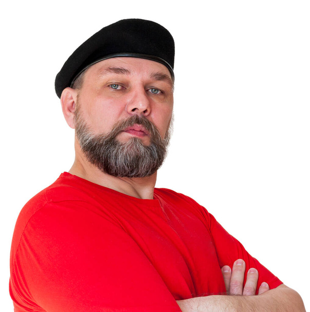 Een man van middelbare leeftijd geïsoleerd op wit. Een man met een grijze baard in een rood T-shirt en een zwarte baret. - Foto, afbeelding