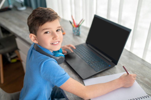 Cheerful pupil sitting at his laptop during online studies - Photo, Image