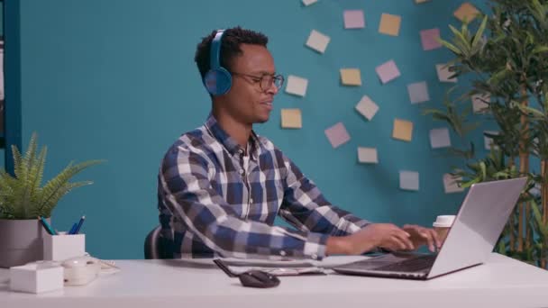 Работник офиса слушает музыку и поет, пользуясь ноутбуком - Кадры, видео