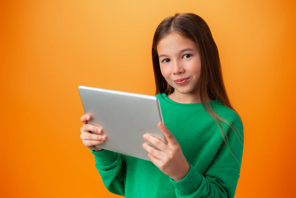 Beautiful teen girl using digital tablet over orange studio background - Foto, Bild