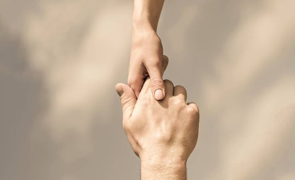 Hände von Mann und Frau, die einander reichen, stützen. Solidarität, Mitgefühl und Nächstenliebe, Rettung. Hilfe leisten. Hände von Mann und Frau auf blauem Himmel. Helfende Hand - Foto, Bild