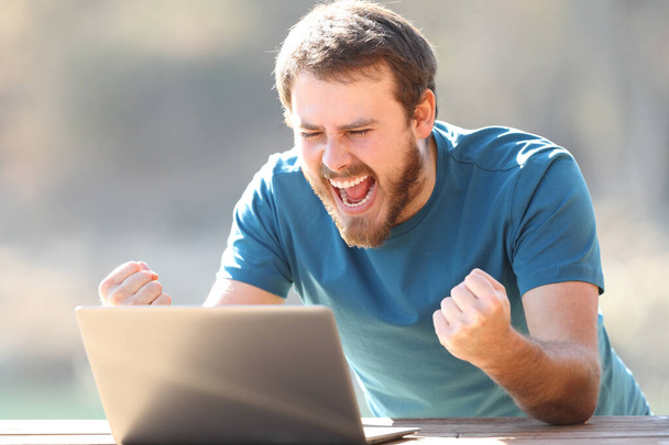Excited man checking laptop content celebrating good news outdoors - Valokuva, kuva