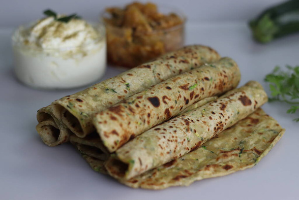 Indian flat bread made of whole wheat flour, grated zucchini and coriander leaves served with spiced yogurt and gooseberry pickle. Shot on white background. Commonly known as Zucchini paratha in India - Photo, Image