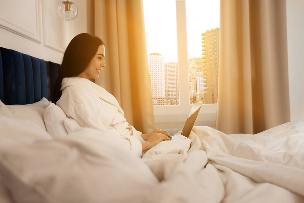 Happy young woman working with laptop on bed in hotel room - Foto, immagini