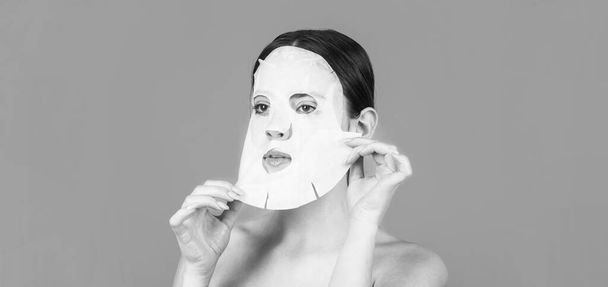Moisturizing mask. Anti aging procedure. Woman applying sheet mask on her face, on blue background. Beautiful woman with mask - Photo, Image