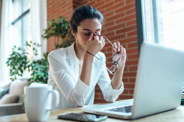 Tiro de mujer de negocios cansado con dolor de cabeza buscando incómodo mientras se trabaja con el ordenador en la oficina - Foto, Imagen
