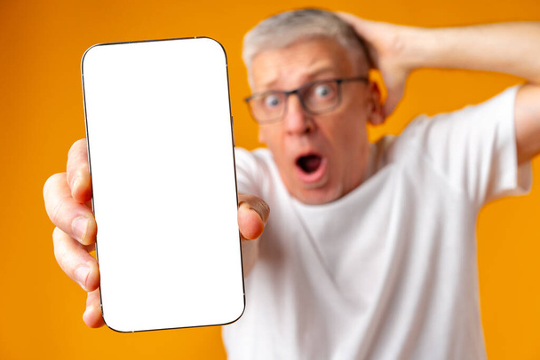 Photo of senior surprised man point finger at smartphone over yellow background - Фото, изображение