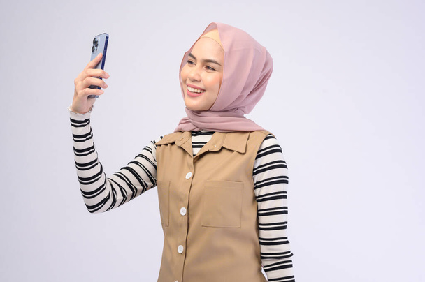 A portrait of beautiful woman with hijab using cellphone on white background - Valokuva, kuva