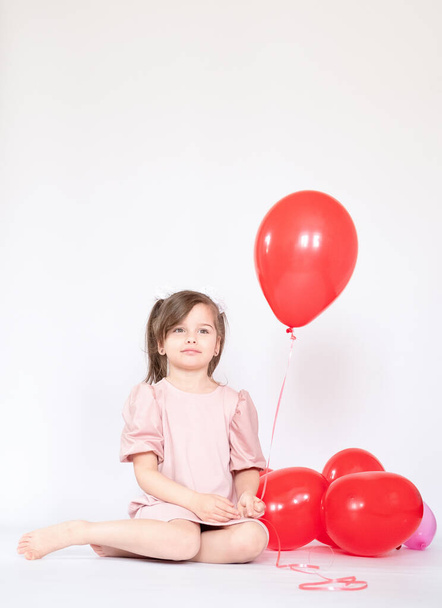 Cute little girl holding a bunch of red heart-shaped balloons - Fotoğraf, Görsel