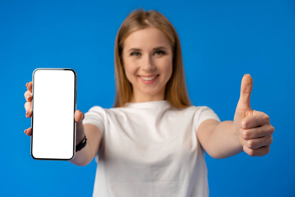 Young woman point finger at isolated smartphone screen over blue color background - Foto, imagen