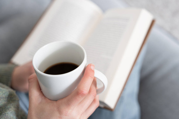Sluiten van de hand houden kopje koffie met een boek over de achtergrond - Foto, afbeelding