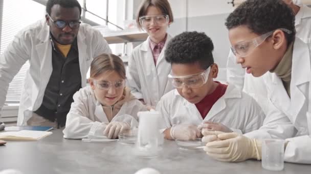 Cintura para cima lentidão de grupo de estudantes diversos e seu professor masculino afro-americano olhando para fumaça de laboratório em frasco durante a realização de experimentos químicos na aula durante a aula de ciências - Filmagem, Vídeo