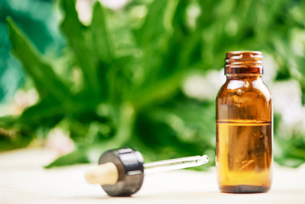 frasco de aceite de cannabidiol para el tratamiento natural de dolores musculares, sobre un fondo borroso de hojas de cannabis - Foto, Imagen