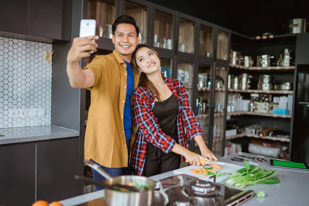 asian couple taking selfie while cooking together in the kitchen - Photo, Image