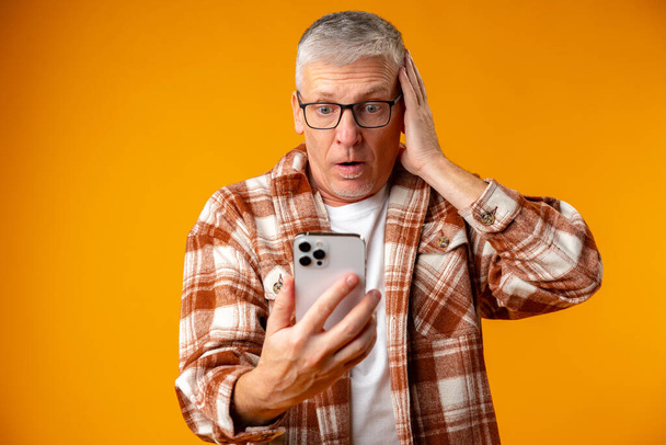Concerned and troubled shocked senior man using smartphone - Foto, Imagen