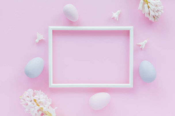 Minimalistic Easter holiday background with pastel colored eggs, photo frame and hyacinth flowers on a pink background. Flat lay greeting card with space for text. - Photo, image