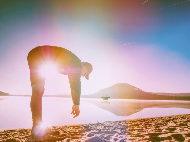 Homme de sport étirant se pencher en arrière sur la plage. Runner exercice au lac. Éclairage abstrait, fusée éclairante colorée. - Photo, image