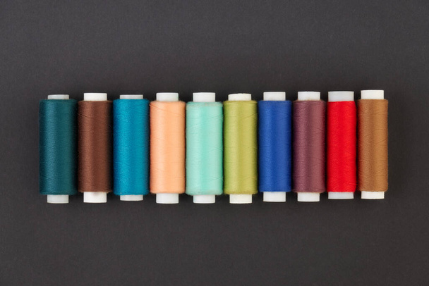 Panoramic detailed view of multi-colored spools of thread on a black background. - Foto, Bild