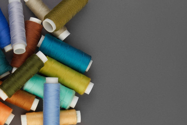 Colored sewing threads are laid out on a gray background, space for text. Top view, copy space. Beautiful background from accessories for tailoring. - Φωτογραφία, εικόνα