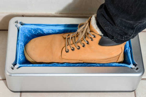 Schuhbezüge und ein Clinthoper, ein Organisator für Einweg-Schuhbezüge im Krankenhaus, ein Mann zieht Stiefelbezüge für Sauberkeit im Zimmer an, eine Maschine für die Montage von Stiefelbezügen. - Foto, Bild