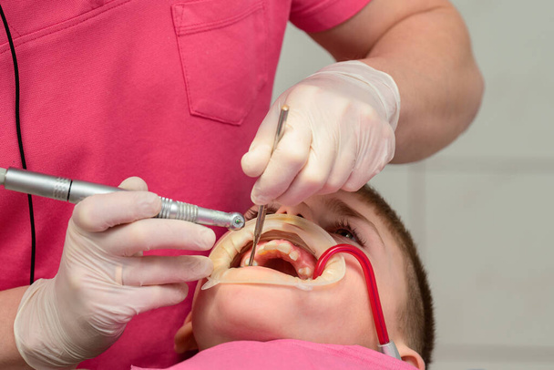 Çocuk dişçi koltuğunda oturuyor, bir çocuğun karnını doyuruyor, dişçi dişlerini matkapla çıkarıyor, beyaz eldivenli dişçi.. - Fotoğraf, Görsel