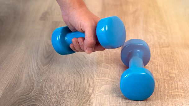 El hombre hace ejercicio con dos pesas azules, preparándose para el entrenamiento deportivo en casa interior. Ejercicios de entrenamiento de fitness en casa. - Foto, Imagen