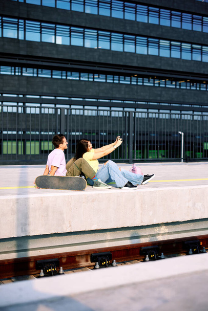Adolescentes sentados en la estación de tren en el exterior urbano y mirando fotos en cámara digital. Adolescentes pasando el rato. - Foto, imagen