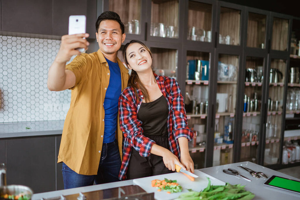 asian couple taking selfie while cooking together in the kitchen - Photo, Image