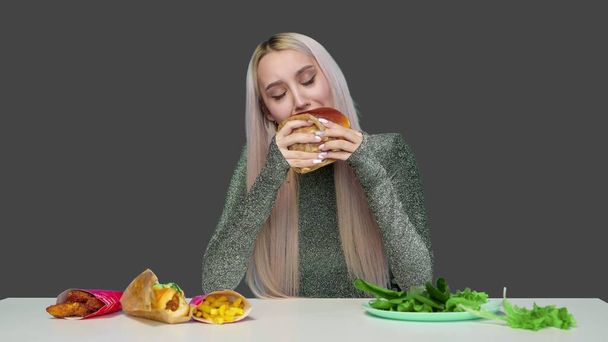 Close-up of a girl with red lipstick on her lips, eating a hamburger on a gray background. Diet. The concept of healthy and unhealthy food. fast food - Photo, Image