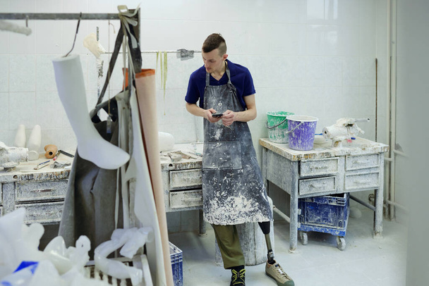 Jeune homme en tablier faisant la révision des fournitures de travail dans l'atelier de l'usine - Photo, image