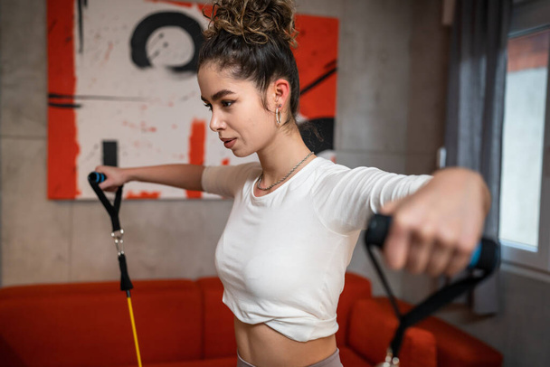 Güzeller güzeli bir kadın, evde lastik direnç bantları kullanarak spor tüpleri kullanarak egzersiz yapıyor sağlık ve zindelik kavramını taklit ediyor. - Fotoğraf, Görsel