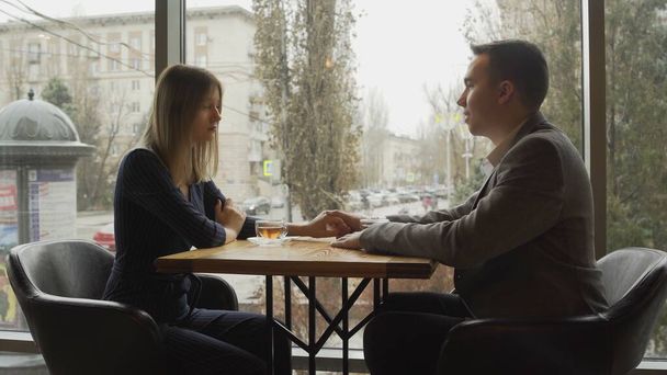 Мужчина и женщина сидят напротив друг друга в кафе или ресторане у окна и общаются. Свидание в кафе или ресторане. Романтическая атмосфера - Фото, изображение