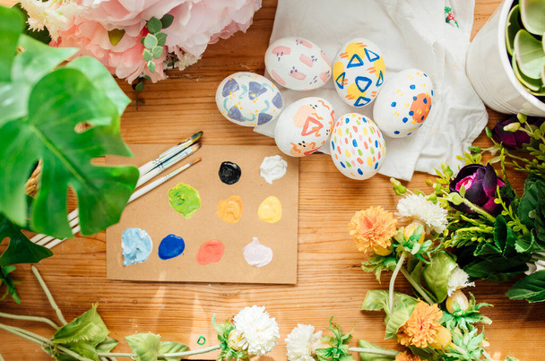 Flat lay of modern easter eggs painted. Brushes and paints with flowers and plants. Happy easter concept on a wooden background. - Фото, зображення