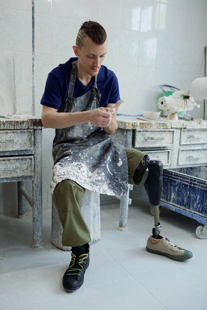 Özürlü genç adam protez atölyesinde küçük bir masada oturuyor. - Fotoğraf, Görsel