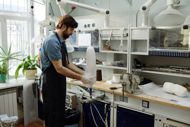 Работник мануфактуры накладывает белый лист на заготовку протезной розетки - Фото, изображение
