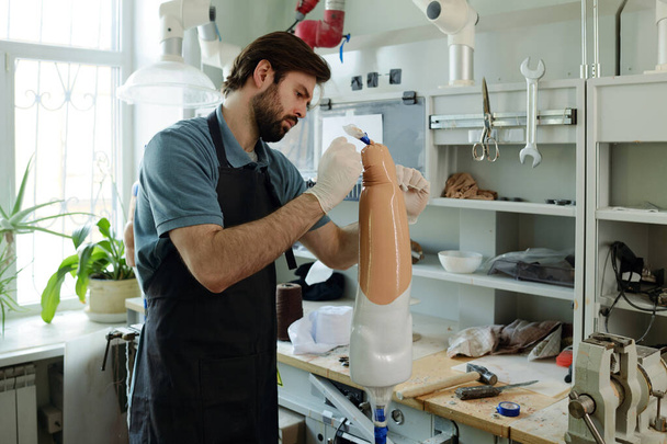 Работник протезного завода накладывает термопластический лист на искусственную конечность - Фото, изображение