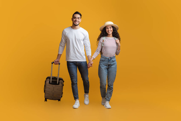 Tempo di ferie. Giovane coppia mediorientale a piedi con bagagli su sfondo giallo - Foto, immagini