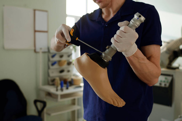 Молодий рукавички ручний працівник складає частини штучної ноги
 - Фото, зображення