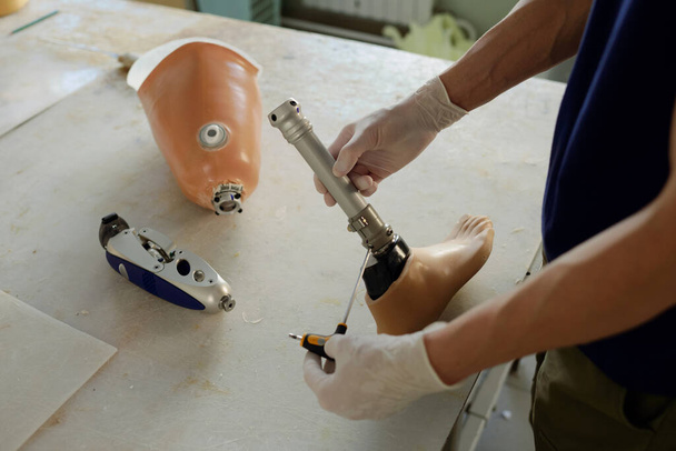 Mains de travailleurs manuels gants tenant un tournevis et une partie de la prothèse de jambe - Photo, image