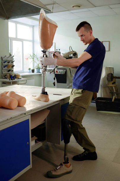 Ручной рабочий с ограниченными возможностями, стоящий за столом во время фиксации частей механизма - Фото, изображение
